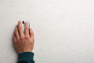 Man using computer mouse on wooden table, top view. Space for text