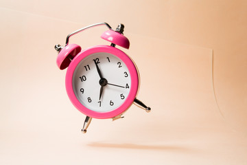 The morning alarm clock jumping up from the bell on a peach background.