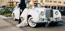 Bride And Groom Next To Classic Car On Street Kissing