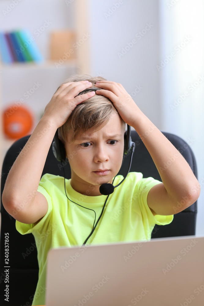 Cute emotional boy playing video game on laptop at home