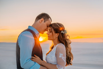 Wall Mural - Unusual wedding photo shoot in the desert. Background white sands at sunset. Happy brunette girl with long hair and a guy touch each other. The picture will fill the love and and the rays of the sun