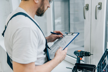 Wall Mural - cropped shot of male handyman writing in clipboard and checking window