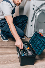 cropped shot of craftsman taking tools from toolbox while repairing washing machine in bathroom