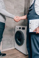 Wall Mural - cropped shot of male handyman with clipboard shaking hands with owner in bathroom