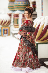 Beautiful happy woman is wearing traditional russian dress in winter park