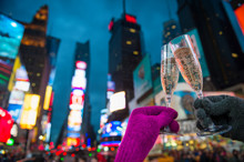 Gloved Hands Holding Up Champagne Glasses In A Mew Year’s Eve Toast Against The Bright Lights Of Times Square, New York City