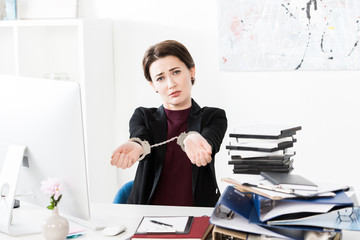 Wall Mural - sad businesswoman showing hands with handcuffs at table in office