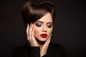 Wall Mural - Beauty Makeup and Hairstyle. Beautiful woman with red lipstick,  long eyelashes, glitter eye shadow and retro hair style, manicured nails isolated on studio dark background.