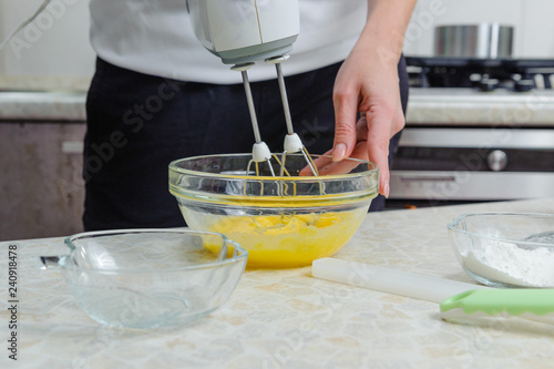 Plakat Kobieta gotuje w swojej kuchni, aby upiec ciasto. Pokonać żółtka z cukrem za pomocą miksera kuchennego