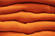 Pile Of Warm Orange Knitted Sweaters In A Row.
