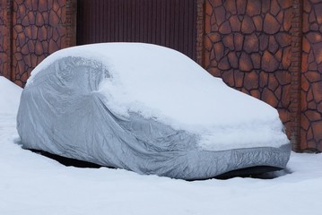 gray tarp covering on a car in white snow near a brown fence