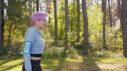 A young y with pink hair jogging in the forest. Medium shot