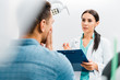 © LIGHTFIELD STUDIOS - selective focus of female dentist standing with clipboard and talking with african american patient having toothache