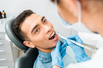 Wall Mural - female dentist drilling teeth of handsome african american patient