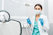 © LIGHTFIELD STUDIOS - female dentist in white coat and mask holding dental instruments