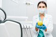 © LIGHTFIELD STUDIOS - female dentist in white coat and mask holding apple