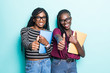 © F8  \ Suport Ukraine - Portrait of two african young school teenage girls thumbs up gesture and holding copybooks and looking at camera isolated over green background