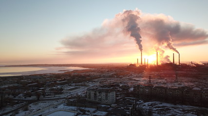 Epic sunset on the background of a Smoking factory. The red sun with bright rays goes beyond the pipe factories and smog. Shooting with the drone. View of part of the city, lake and industry. Red sky.