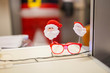 © andrea - horizontal image with detail of a pair of red glasses decorated with Christmas puppets, laid on a white shelf of an office