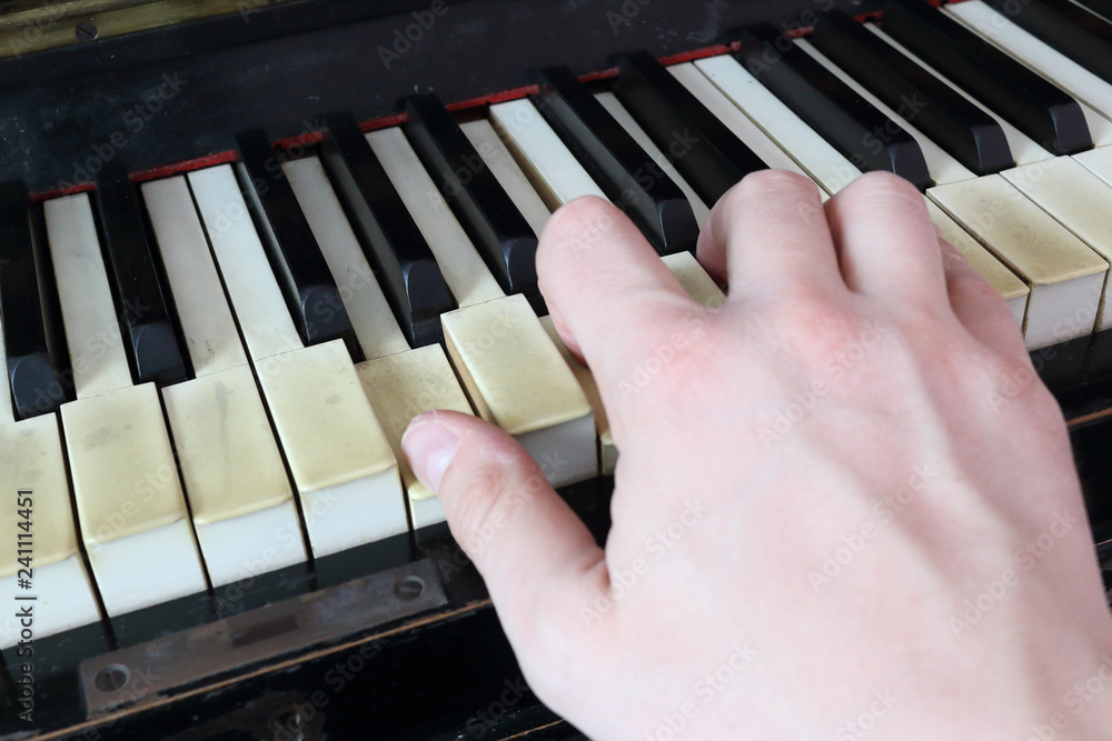 A right hand playing a G (SOL) major chord on an old black piano with yellowed cracked keys, pressing the G (SOL), B (SI), D (RE) notes - obrazy, fototapety, plakaty 