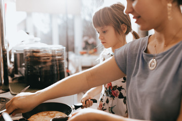 Wall Mural - Mother and her little daughter cooking pancakes for the breakfast in the little cozy kitchen