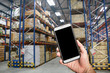 © 9kwan - Hand holding a smartphone at warehouse (Blur background), Concept for logistics management with technology