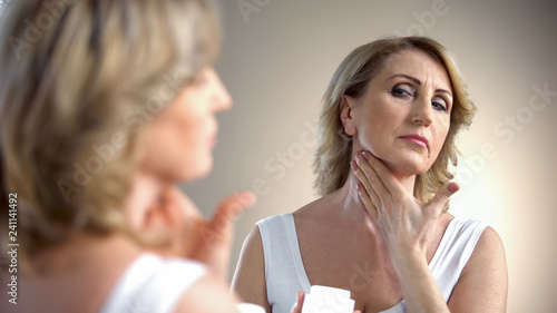 Fotografía Elderly lady applying anti-age cream on neck, skin care in old age, wrinkles