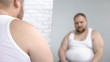 © motortion - Obese man looking at his mirror reflection, overweight problem and insecurities