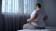 Hulking fat man stretching muscles in morning on bed, suffering from back pain
