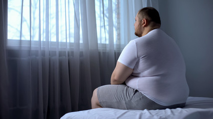 Sad heavy man sitting on bed at home, health problem, depression, insecurities