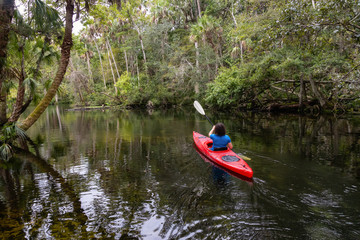 Adventurous girl kayaking on a river covered with trees. Taken in Chassahowitzka River, located West of Orlando, Florida, United States.