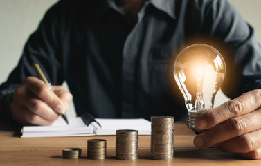 Business man holding light bulb and some coins on table writing  saving bank and account for his money all in finance accounting concept.