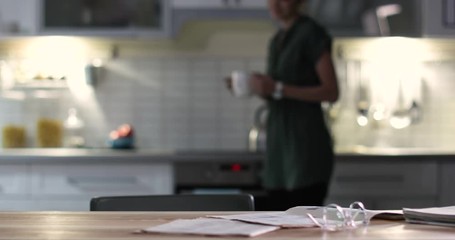 Canvas Print - Beautiful young woman with coffee reading newspaper at table in kitchen
