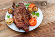 Grilled pork meat with onion, tomato and parsley in white plate on wooden table