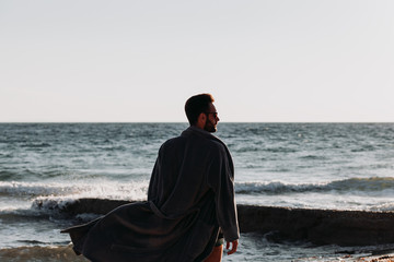 Wall Mural - Young man in a bathrobe on the beach in sunset