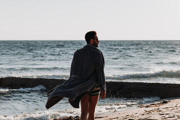 Wall Mural - Young man in a bathrobe on the beach in sunset