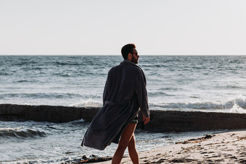 Wall Mural - Young man in a bathrobe on the beach in sunset