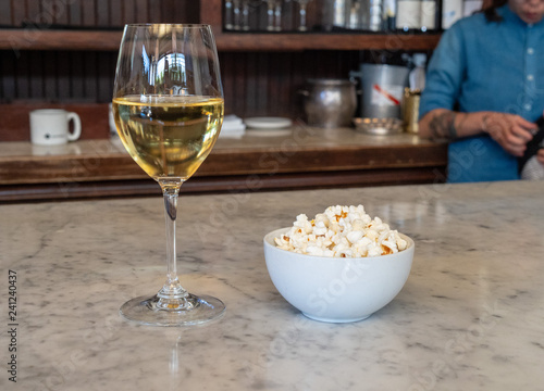 Fotografie, Obraz Wine glass filled with white wine standing next to a bowl of fresh popcorn with