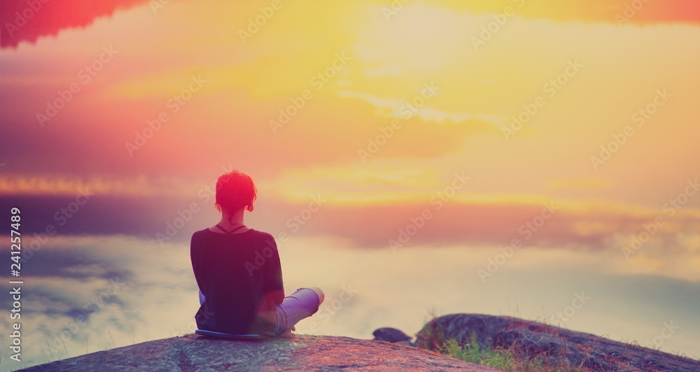 Young woman sitting enjoying peaceful moment of beautiful colorful sunset. In the reflection of the lake water sees clouds and sun. Vintage mood, concepts of winner, freedom, happiness. - obrazy, fototapety, plakaty 