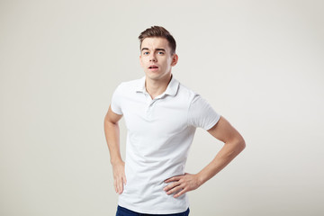 Nice guy dressed in a white t-shirt and jeans keeps his hands on the waist on a white background in the studio