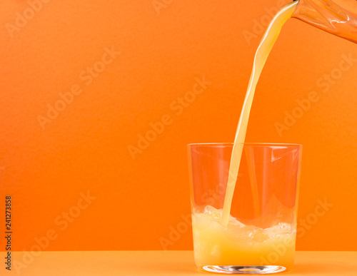 Fotografia orange juice pouring in glass from a jug, isolated on orange background, copy sp
