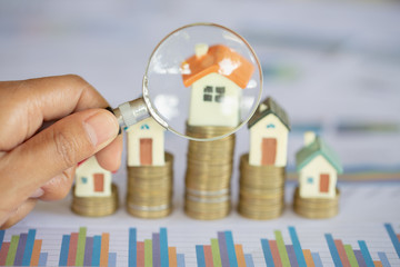 Wall Mural - Close-up Of A Businessperson's Hand Looking At House Model Through Magnifying Glass, House searching concept with a magnifying glass