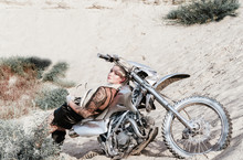 Young sexy girl biker lying on her her silver motorcycle at sand dunes
