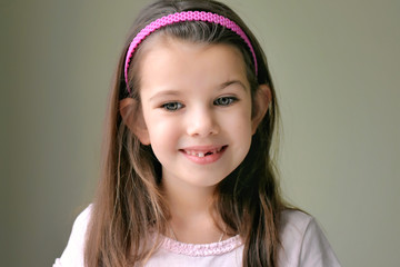 Caucasian white beautiful long haired brunette toothless girl with pink hair band. Smiling cute kid without front milk tooth. Kid expression portrait with fun happy face, who lost his first tooth.