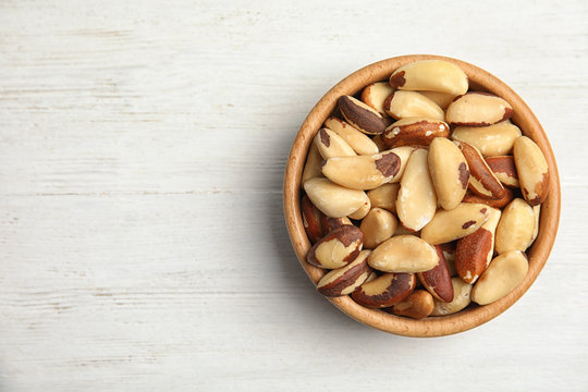 Bowl with tasty Brazil nuts and space for text on white wooden background, top view