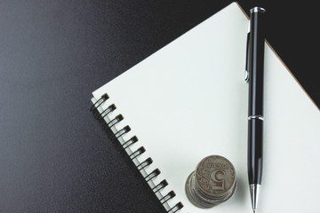 notebook and pen with coins on a wooden table