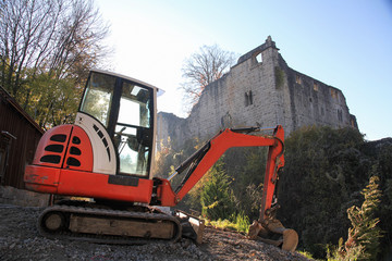 Minibagger auf einer Baustelle mit einer Burgruine im Hintergrund