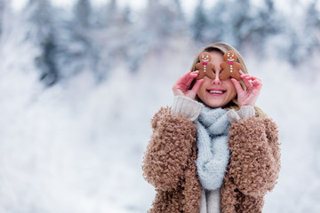 Beautiful girl in coat with cookie in a snow forest. Christmas of Valentine Day season time