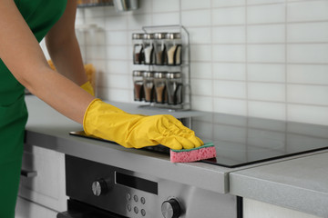 Wall Mural - Female janitor cleaning kitchen stove with sponge, closeup