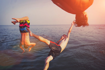 Group of happy people having fun jumping in the sea water from the yacht. Friends in mid air on a sunny day summer pool party. Vacation , friendship , youth concept.